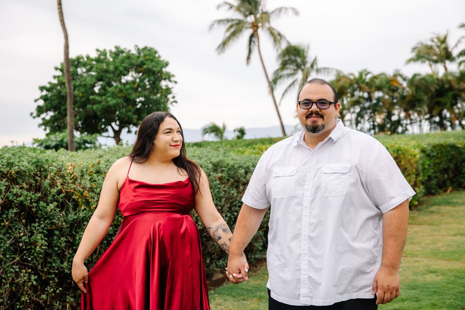 A couple strolls through a lush tropical garden setting near the ocean.