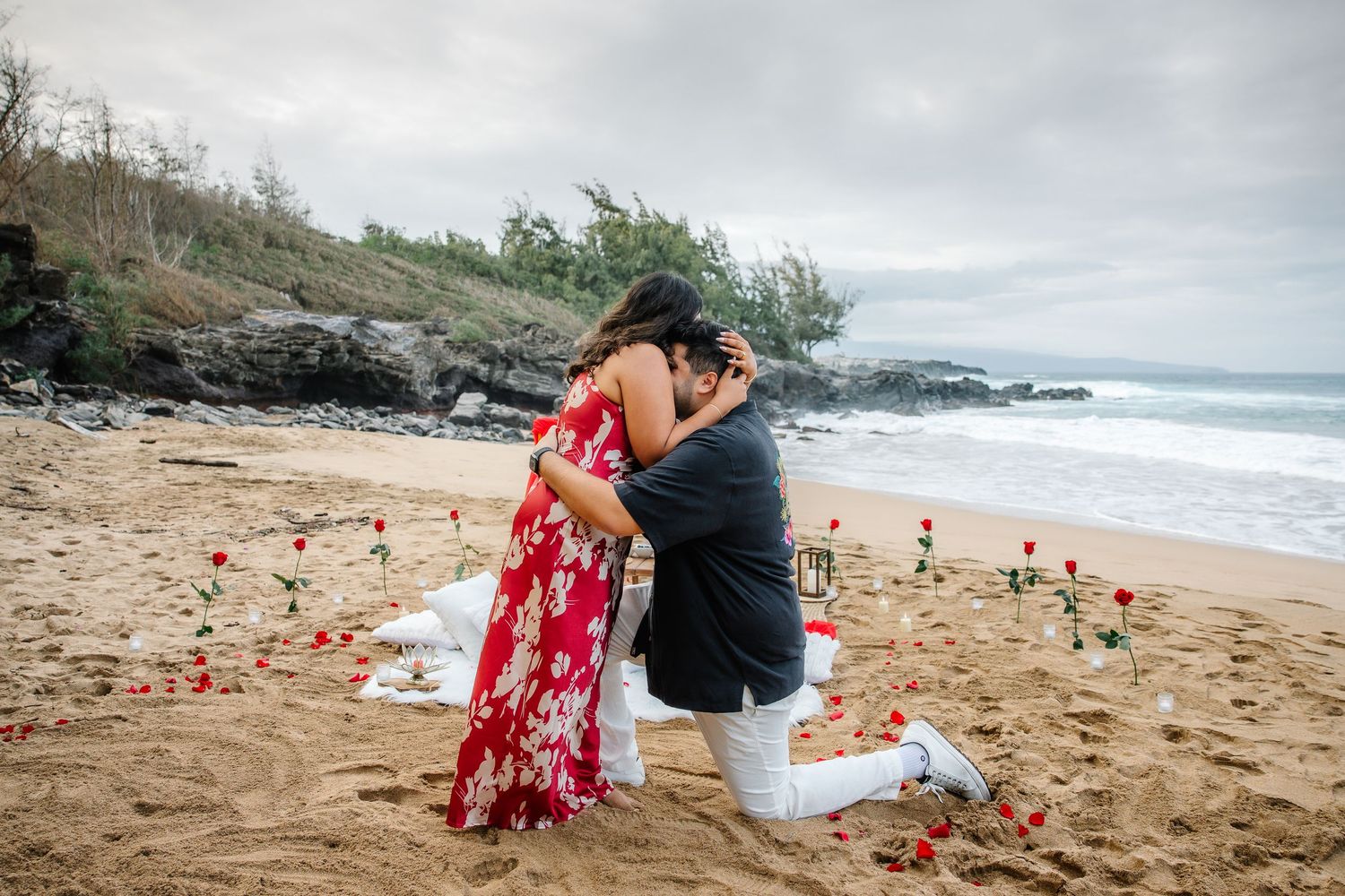 A scenic beach proposal moment with rose petals and ocean waves in the background.