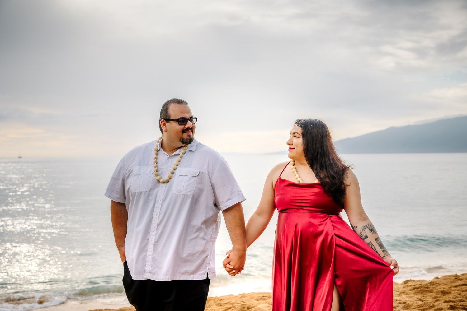 A couple in red and white outfits walks along a scenic coastal path.