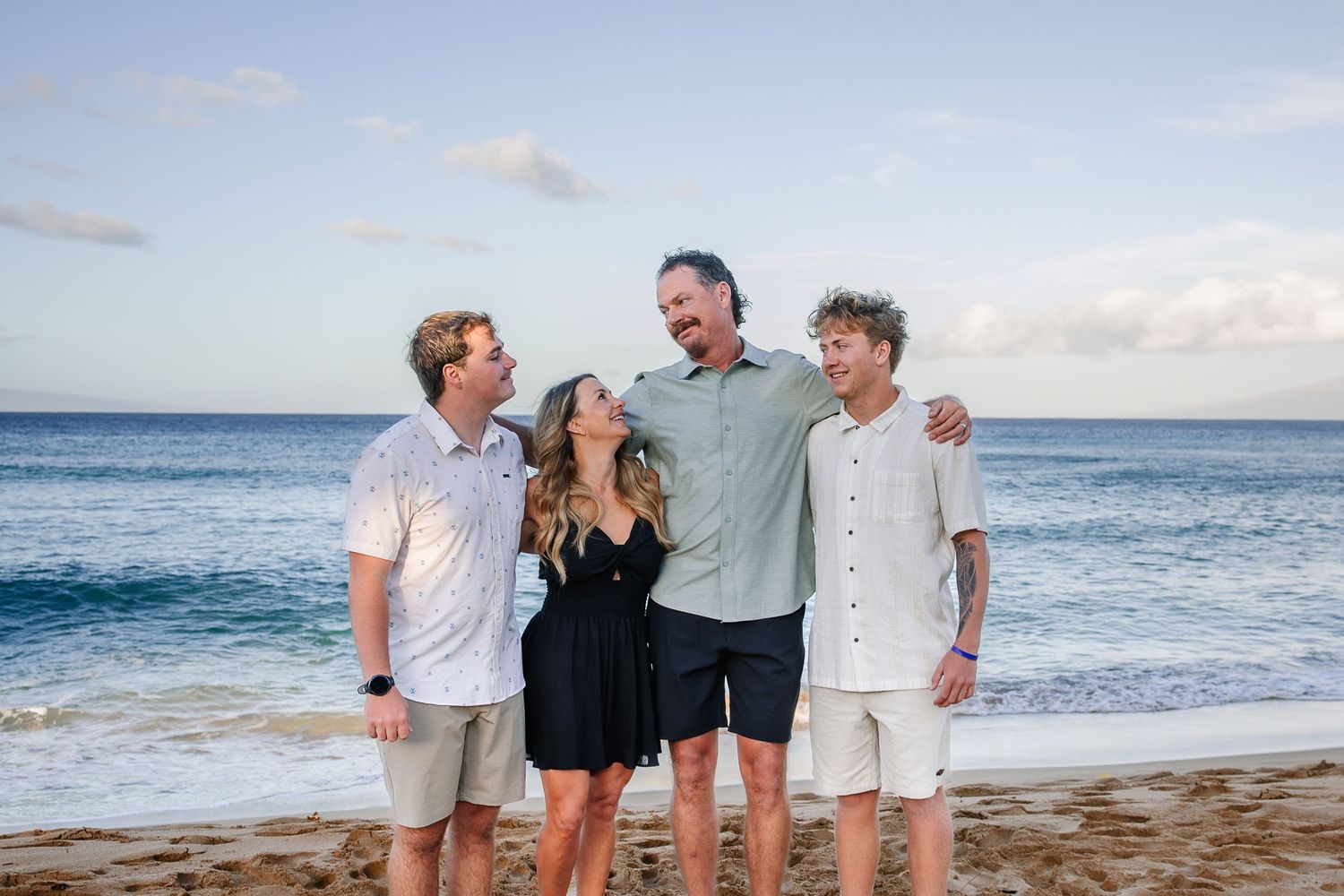 Group portrait session on sandy beach with ocean waves and blue sky in background.