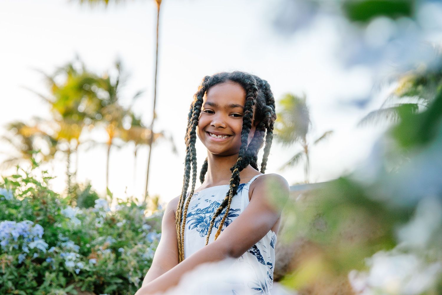 A person in a floral dress poses outdoors during golden hour with soft bokeh lighting effects in the background.
