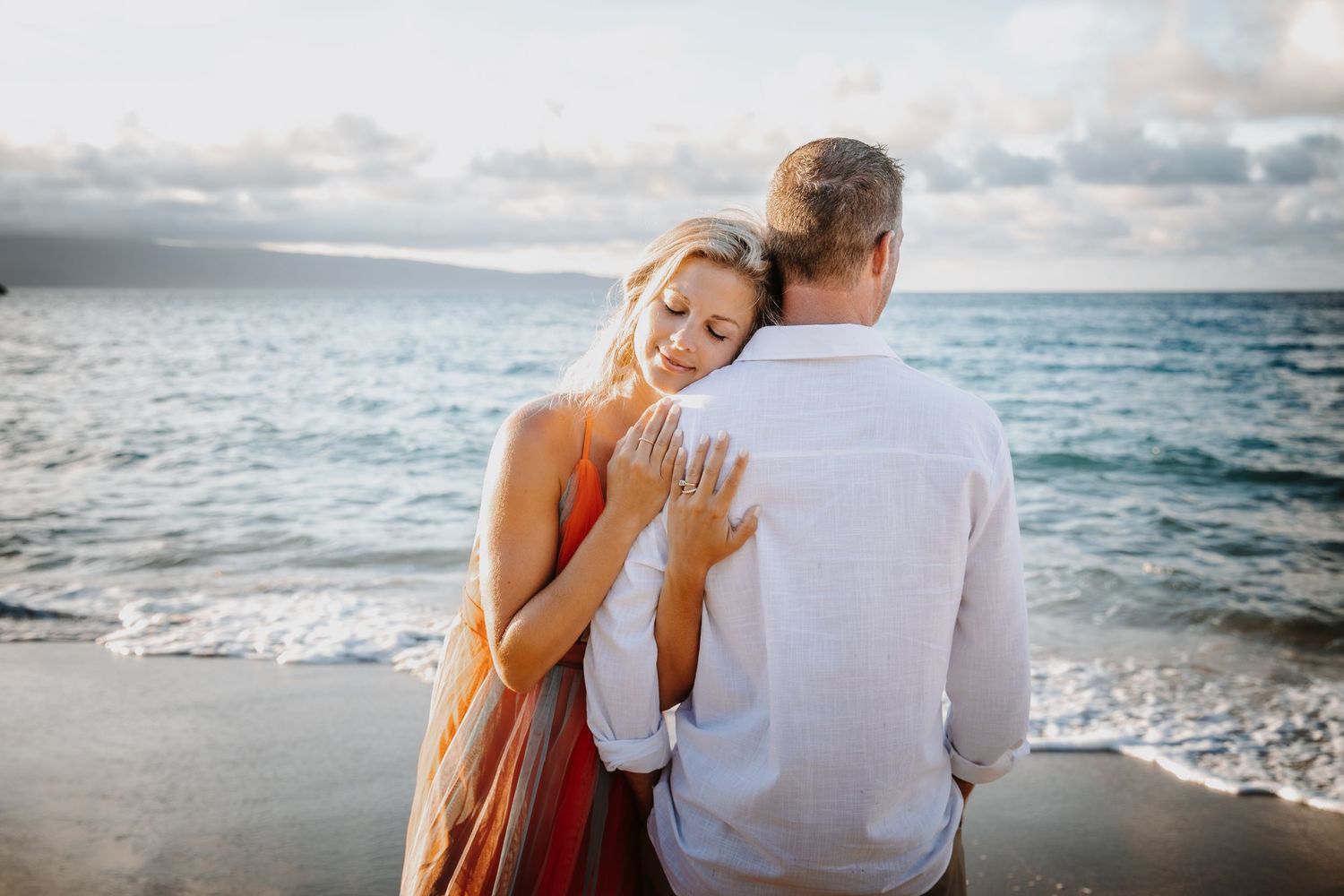 A couple sharing a tender moment on a beach with waves crashing behind them.