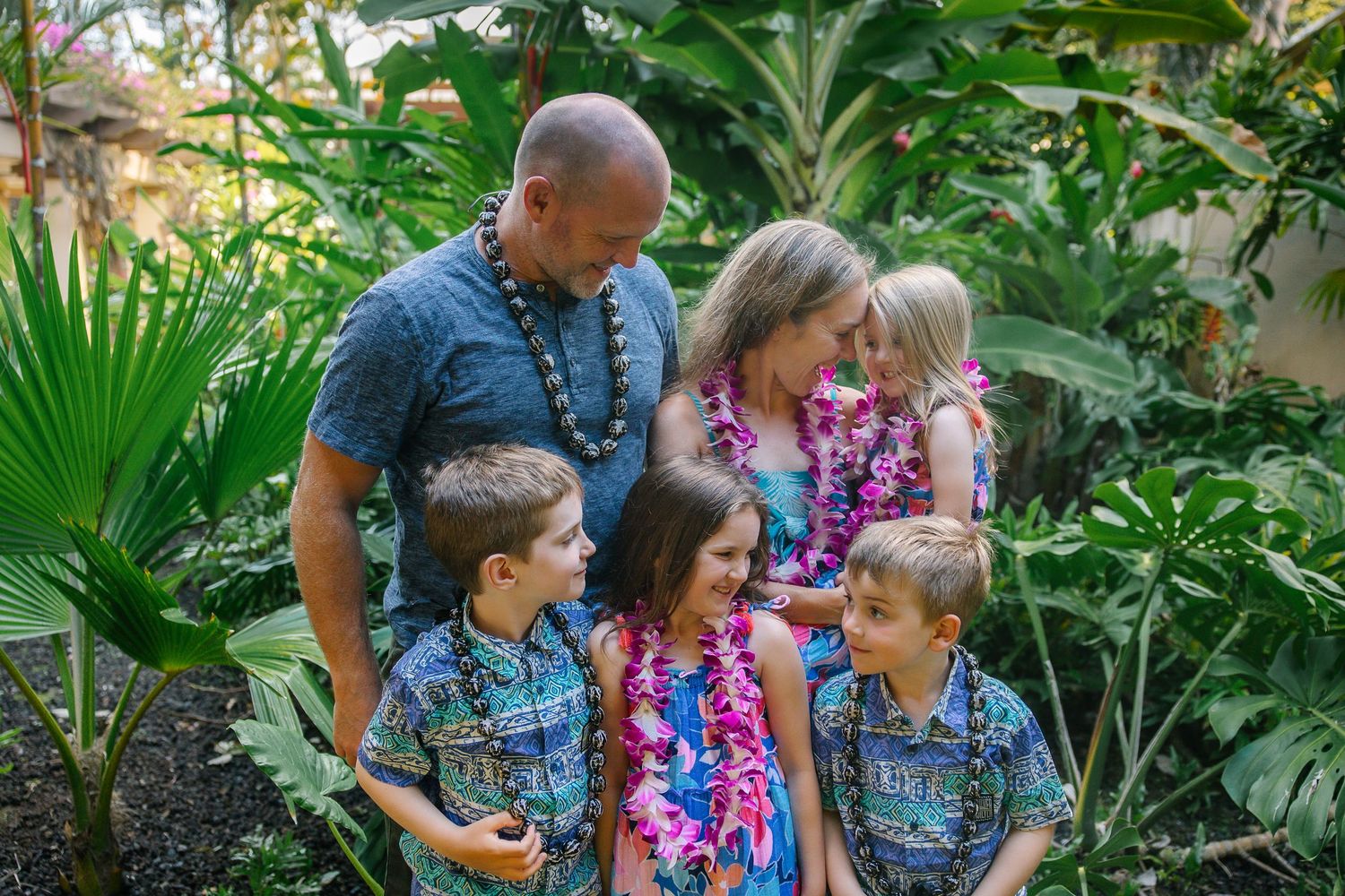 Family group poses in a lush tropical garden setting wearing coordinated blue and floral outfits.