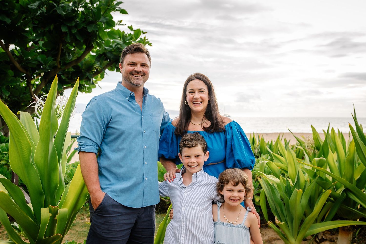 Family posing together in blue outfits against a tropical garden backdrop.