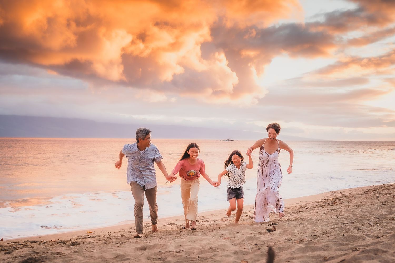 A group of people walking along a sandy beach at sunset with dramatic orange and pink clouds in the sky.