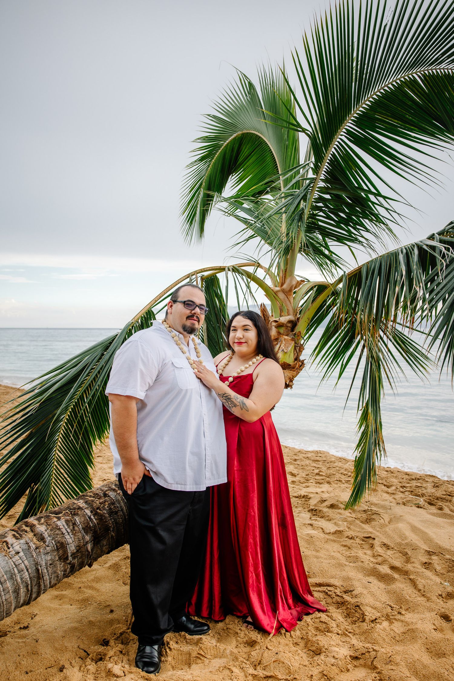 Romantic beach photoshoot with palm trees featuring a couple in red and white formal wear.
