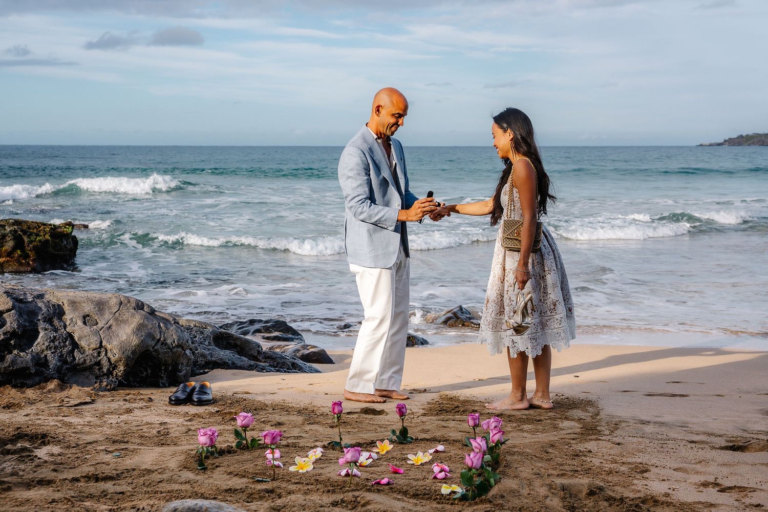 Couple sharing romantic moment on Hawaiian beach with waves and rose petals.