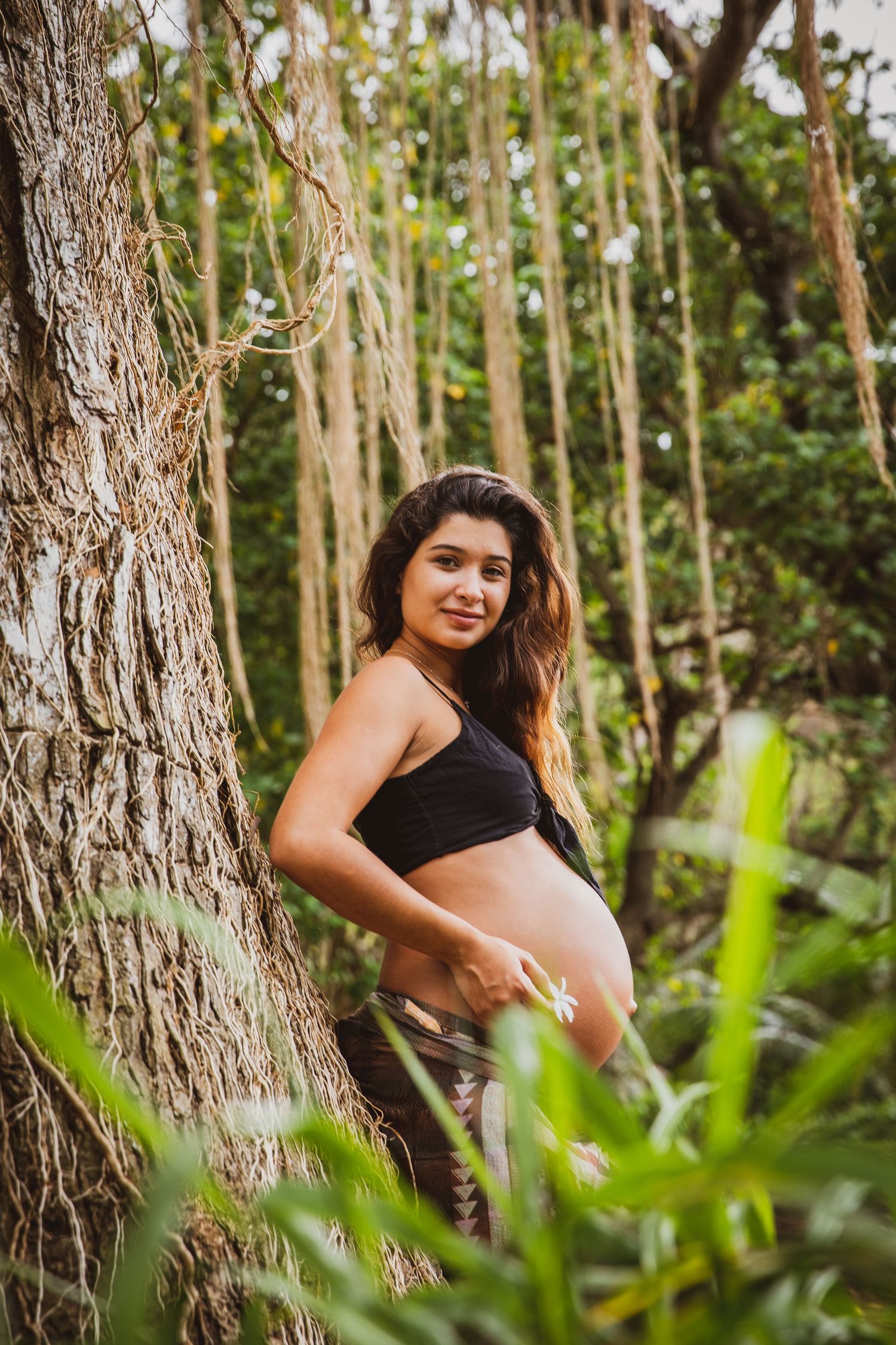 Maternity photography session in a tropical forest with palm trees creating natural framing.