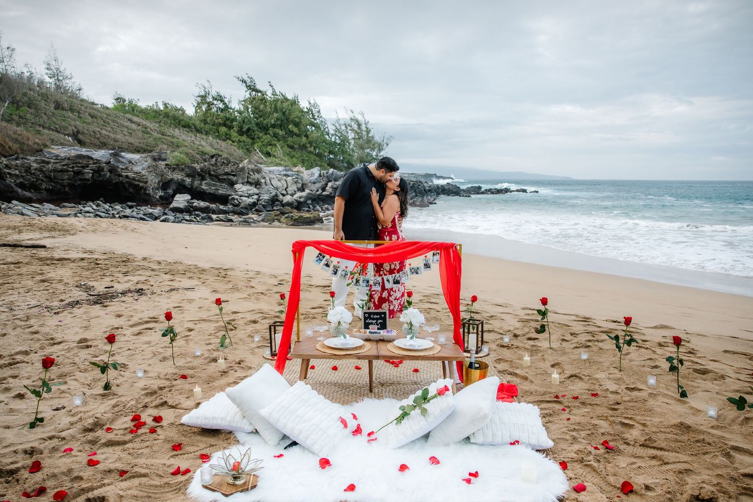 A decorated beach proposal scene with red banners and photo memories displayed.
