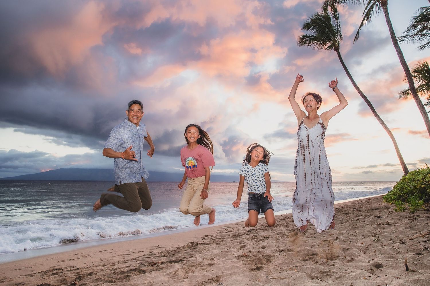 A joyful beach scene at sunset with people jumping and playing on a Hawaiian shoreline with palm trees.