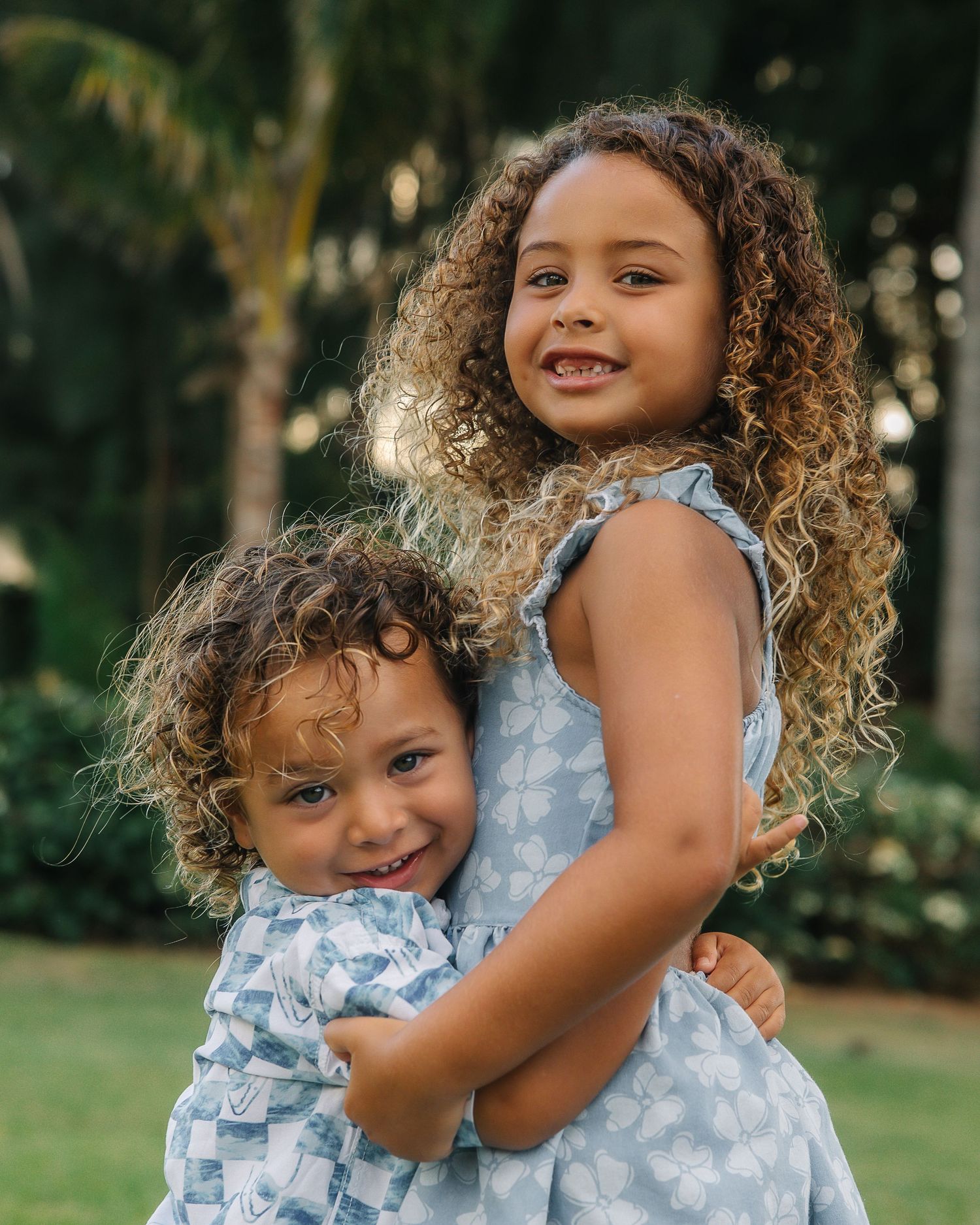 Two young sisters in matching blue dresses share loving embrace outdoors.