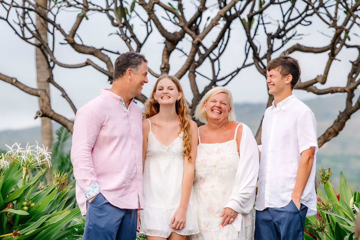 Happy family of four smiling together outdoors near tropical trees and lush greenery on a sunny day.