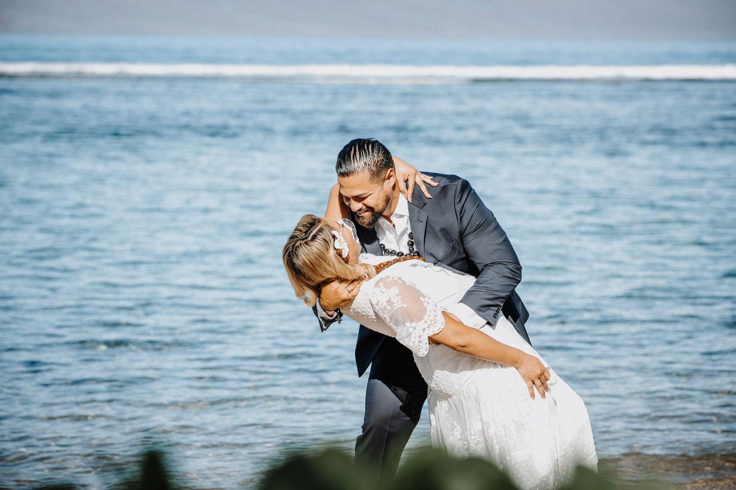 Bride and groom share a romantic dip kiss on a scenic ocean beach during their wedding celebration.