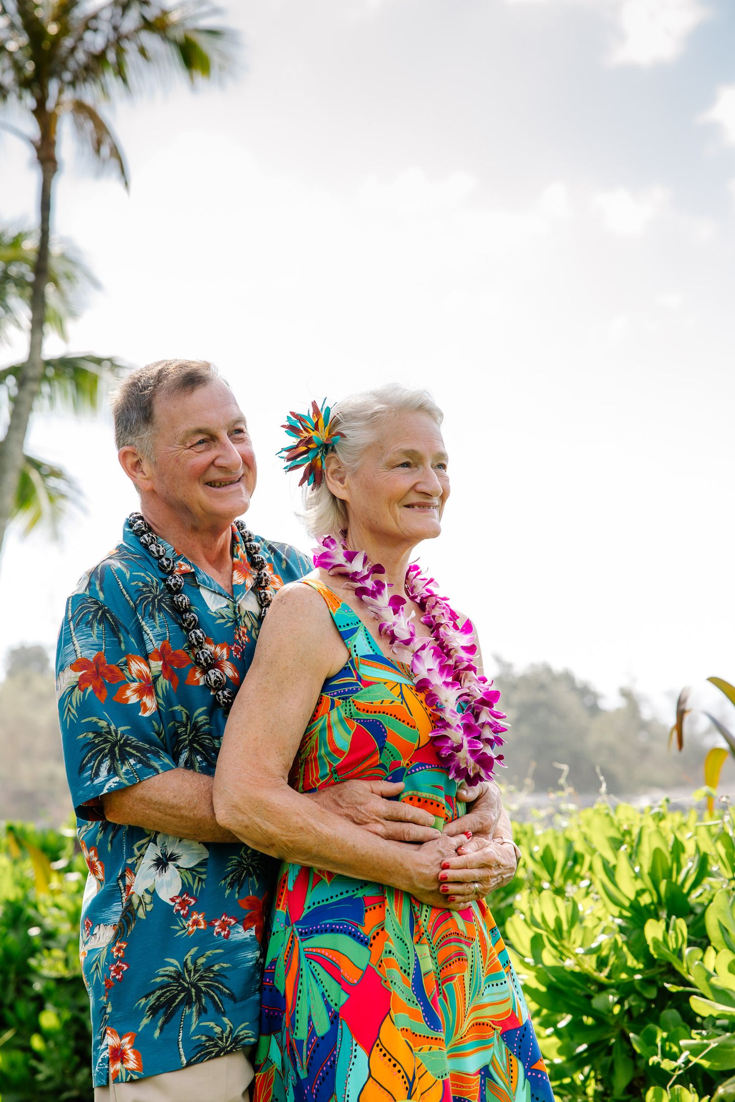A couple in vibrant Hawaiian prints shares joyful moments among tropical foliage.