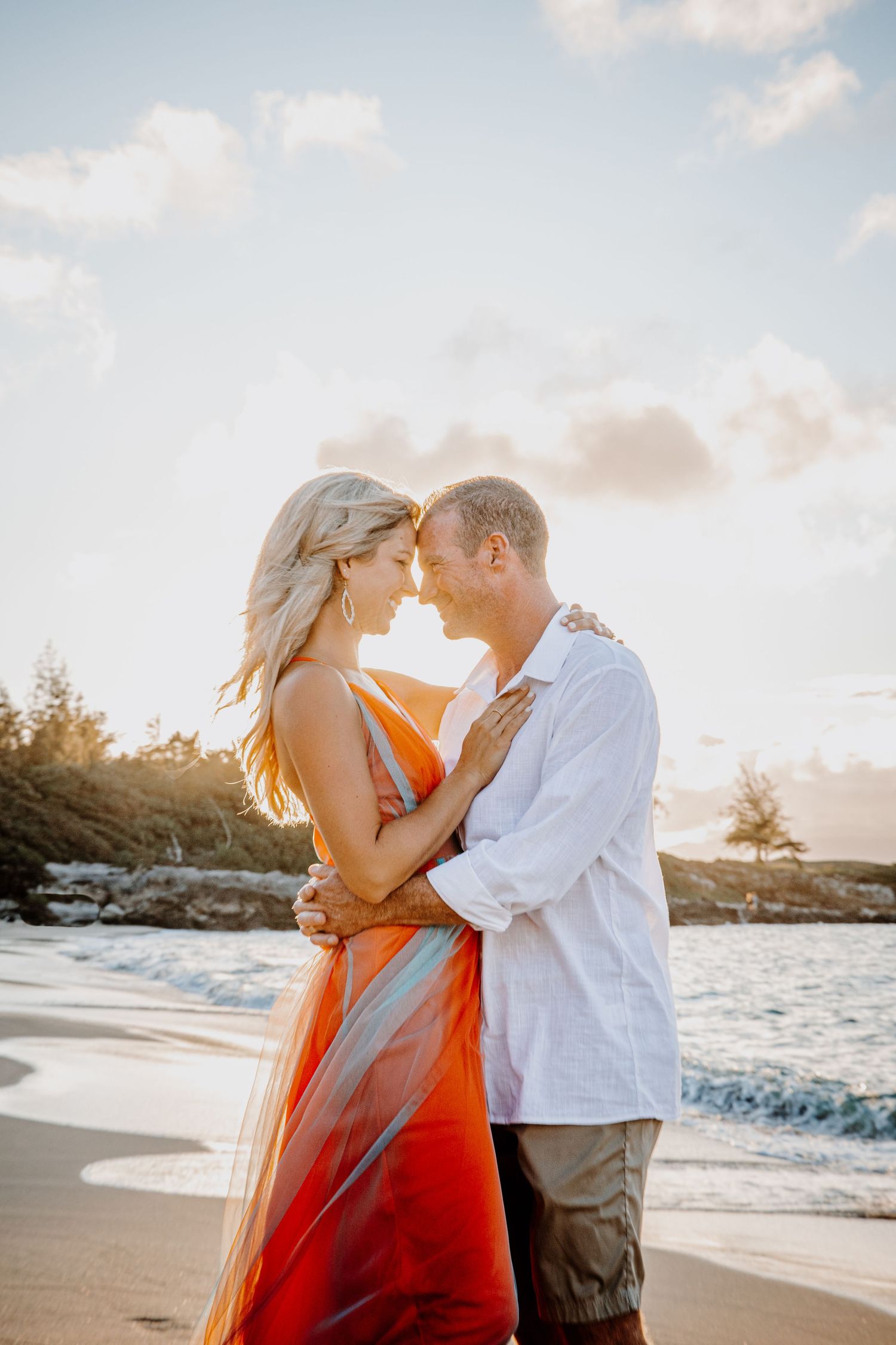 Intimate beach photoshoot with couple in orange dress and white shirt at sunset.