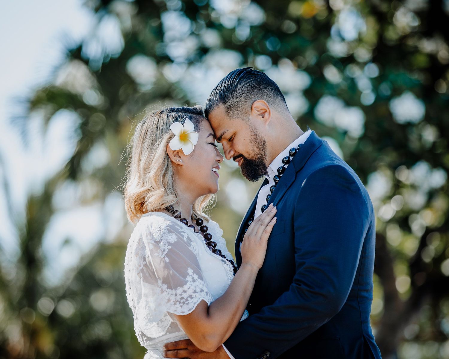 A romantic wedding portrait with a flower in hair against a tropical green background.
