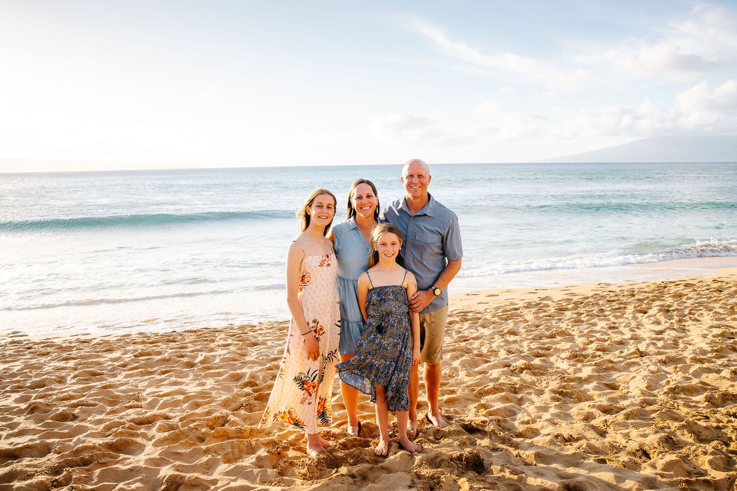 A group poses together on a sandy beach at sunset with ocean waves in the background.