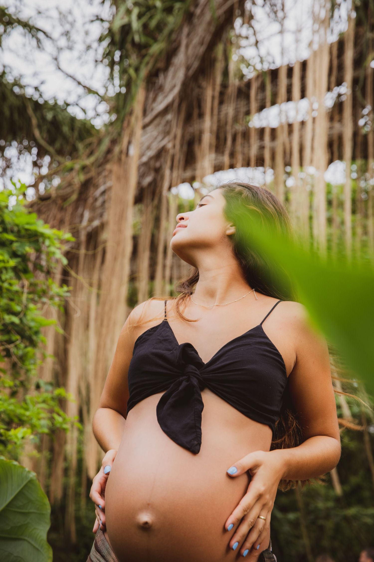 Maternity photoshoot in a wooded area with woman wearing black top and patterned skirt.