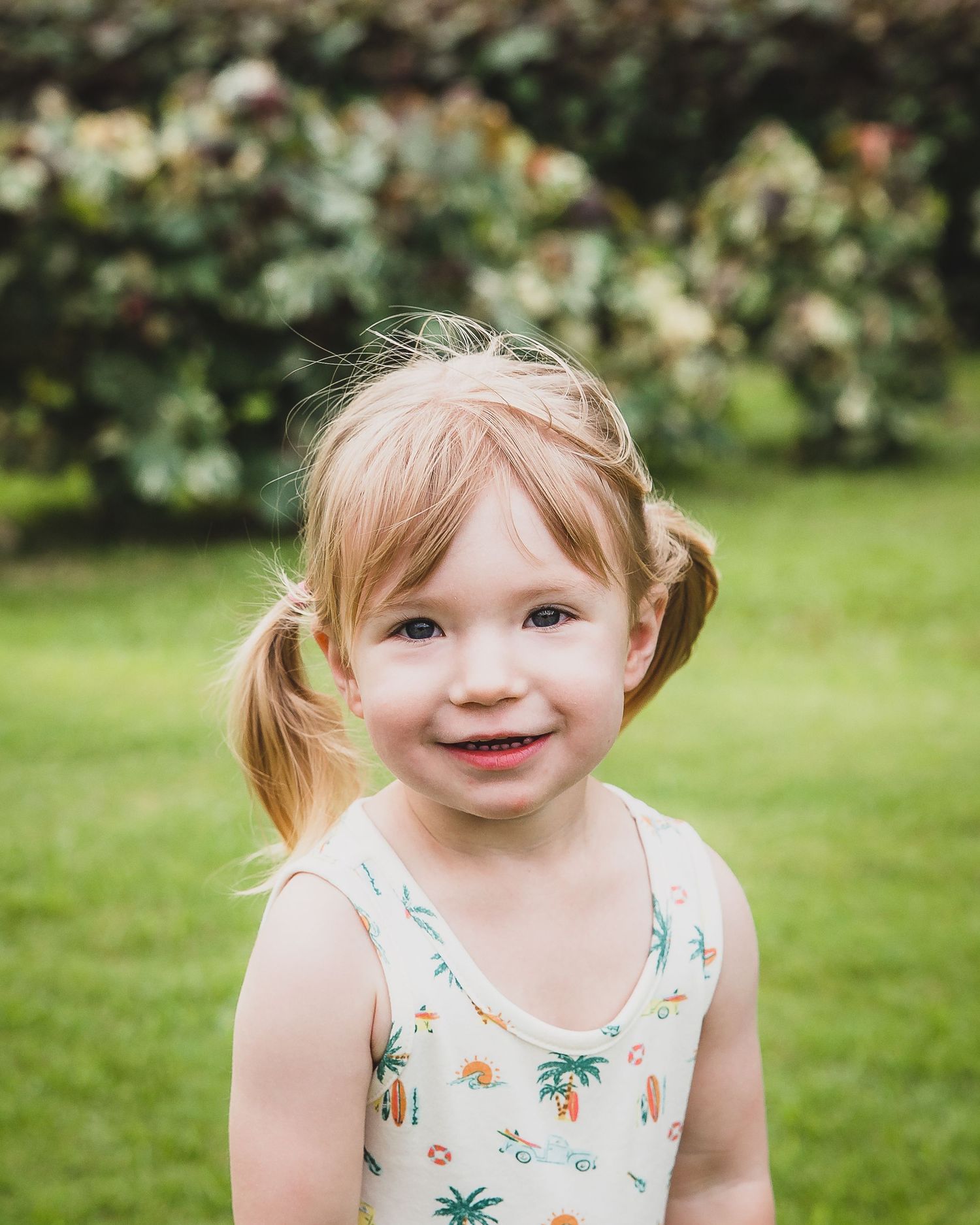 Child wearing a floral summer dress plays joyfully in a lush green garden setting.