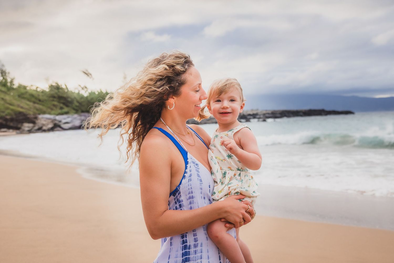 Mother and child share a playful moment together on a scenic Hawaiian beach.