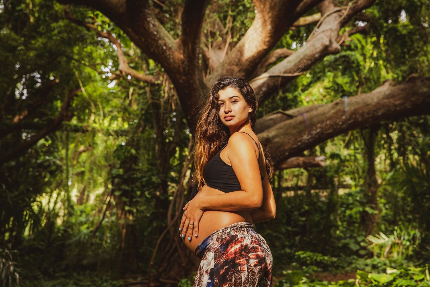 Artistic maternity photos taken in a forest with natural sunlight filtering through trees.