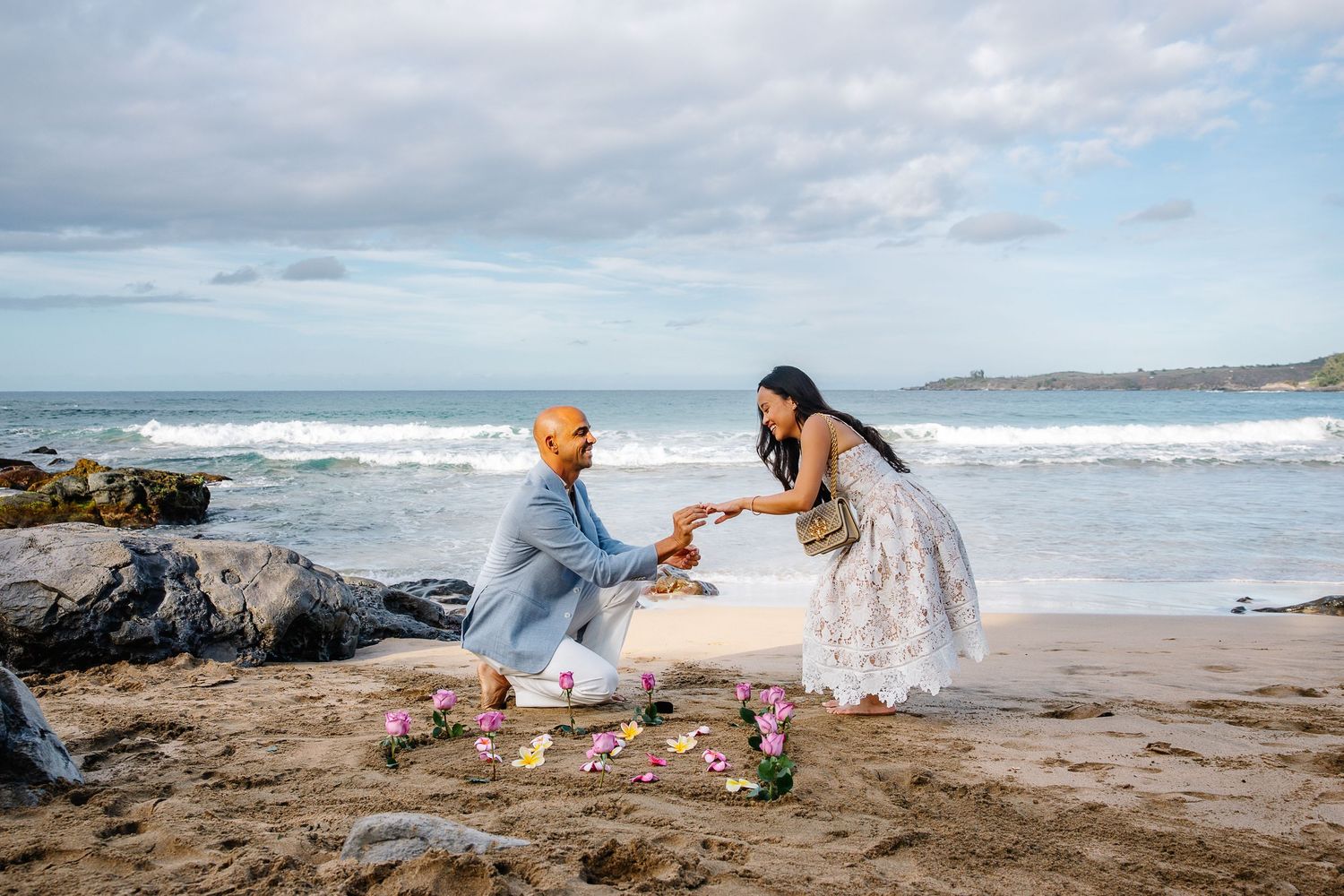 Surprise beach proposal with flower petals and ocean waves in the background.