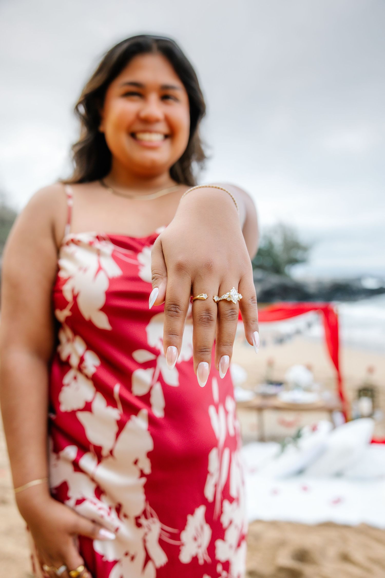Close-up of hands showing off new engagement ring against a red floral dress.