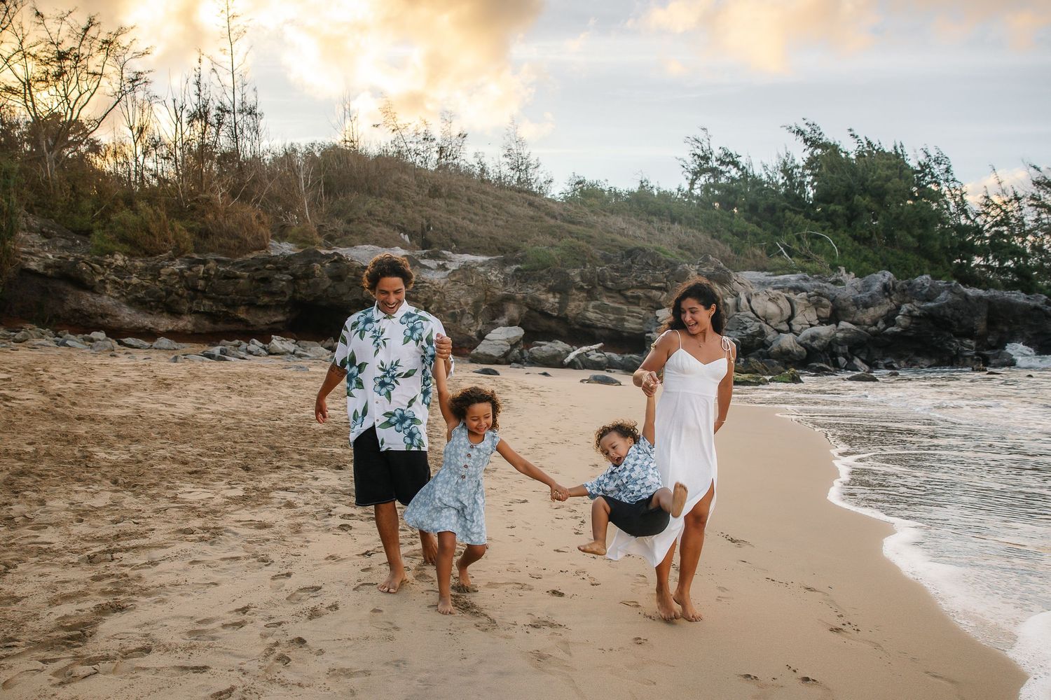 Family walking together along a scenic beach shoreline during golden hour as waves gently roll in.