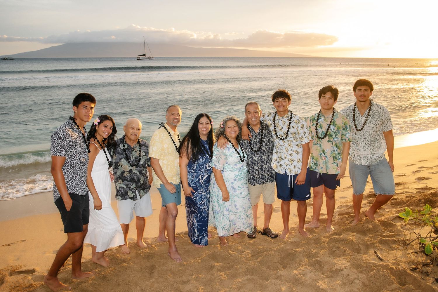 Family group photo on a Hawaiian beach at sunset with mountains and ocean in the background.
