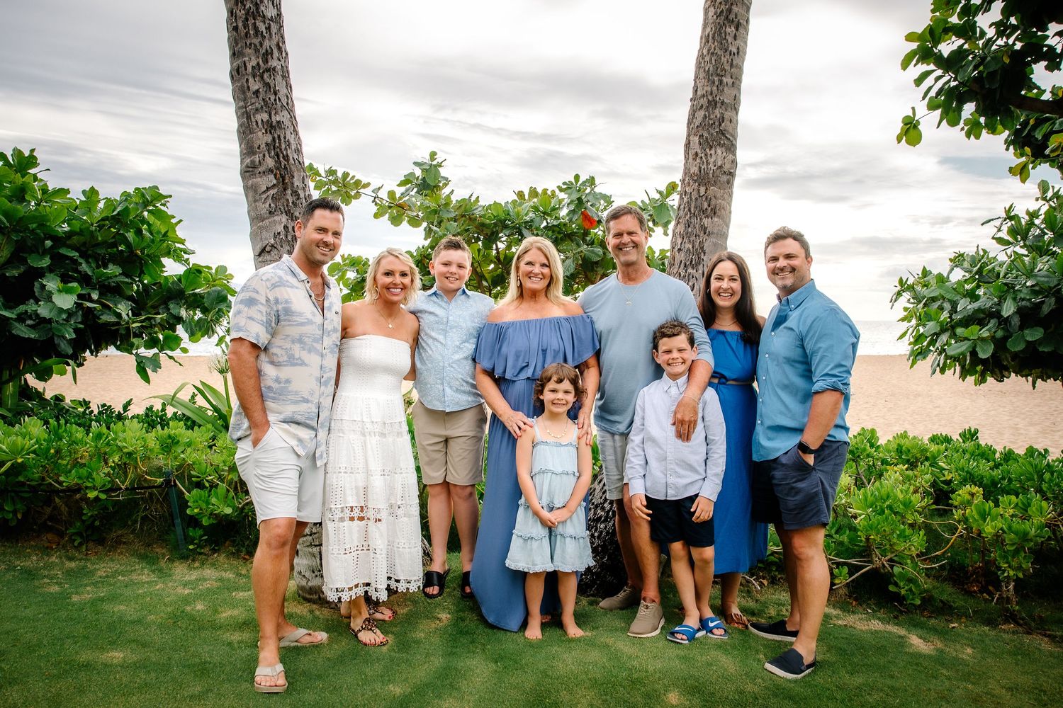 Extended family group portrait on a lush tropical lawn with palm trees.