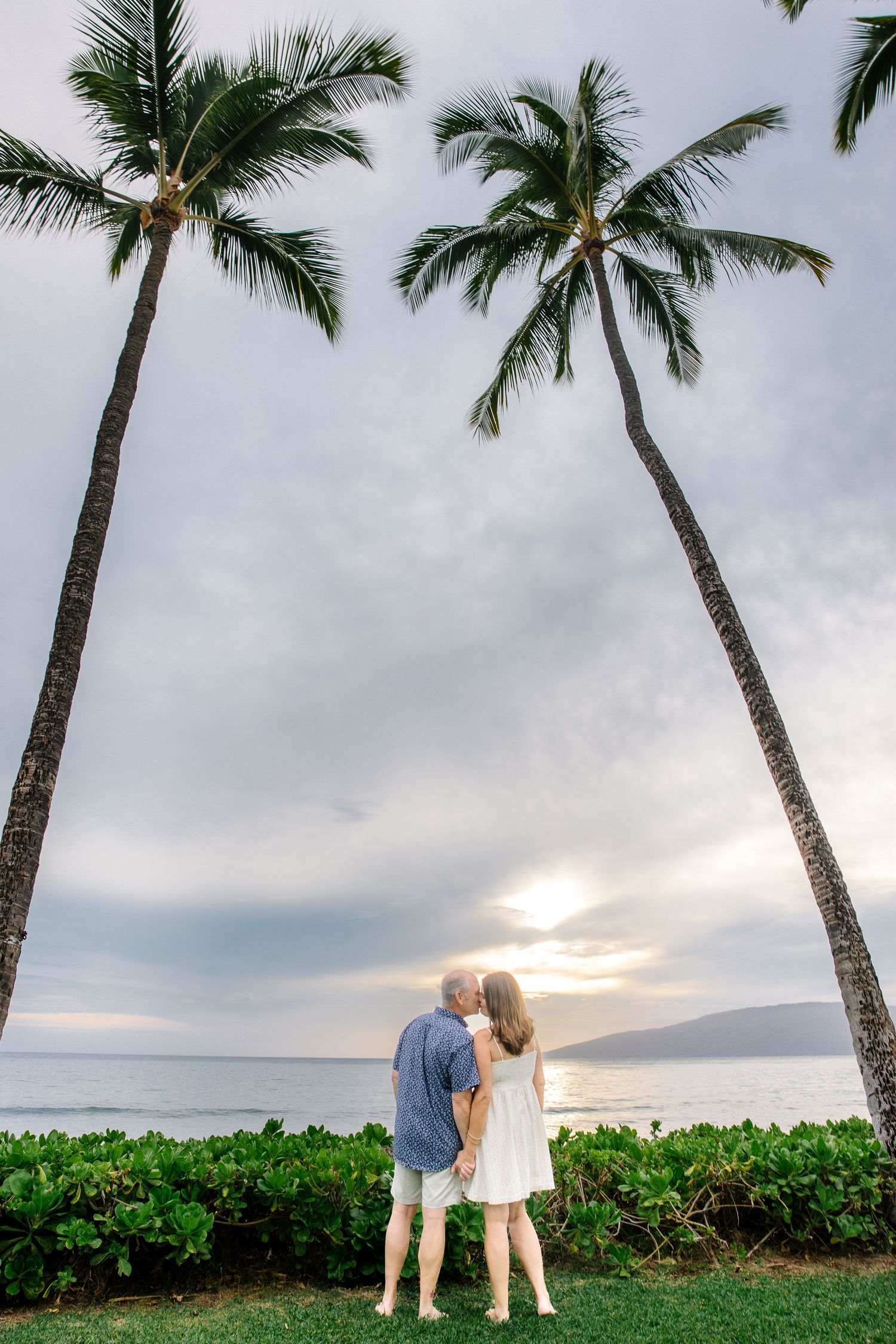 Palm trees frame a romantic beach photoshoot at sunset in Maui with lush tropical landscaping.