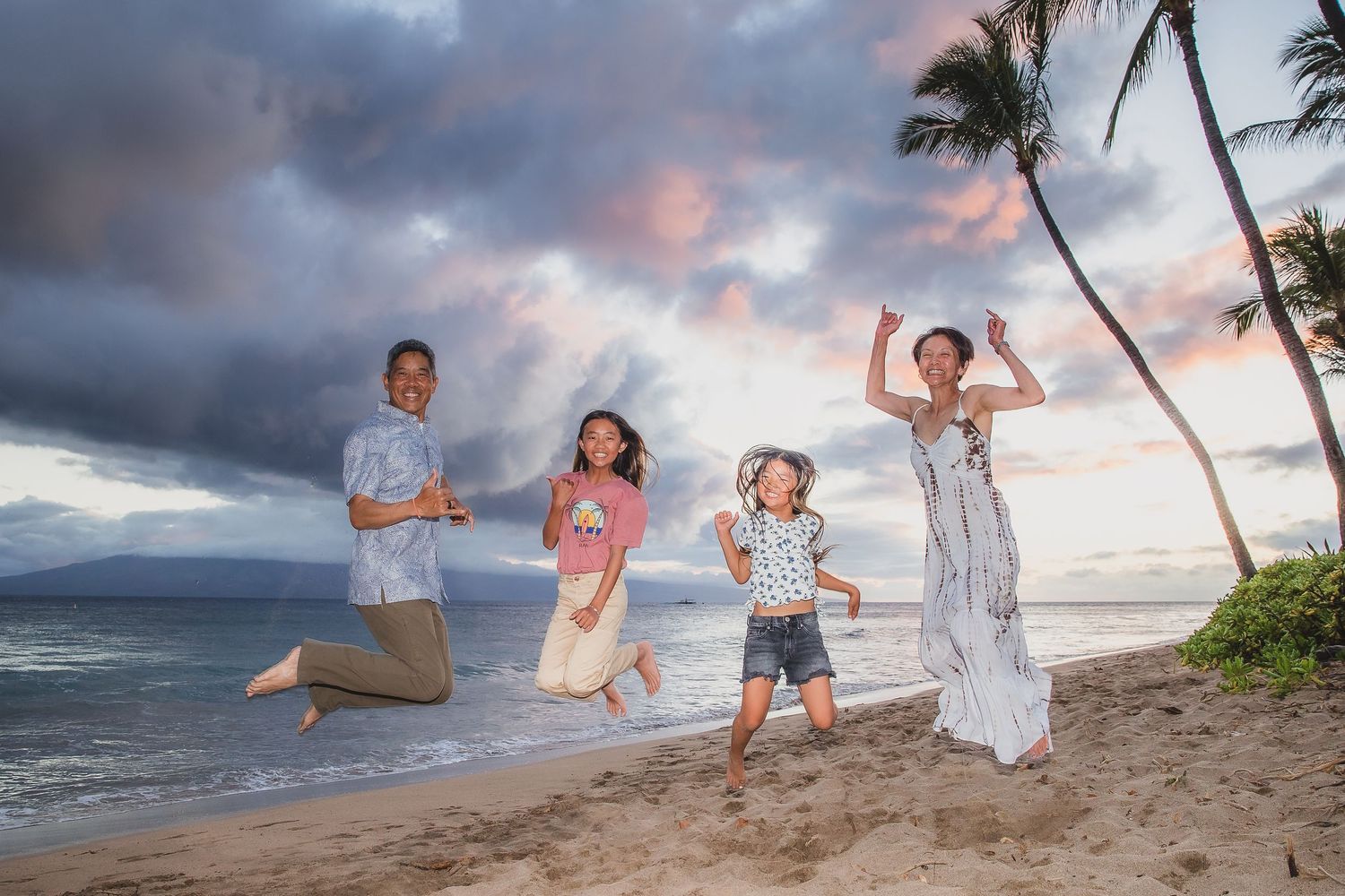 Group enjoying playful moments on beach with dramatic stormy sky and palm trees.