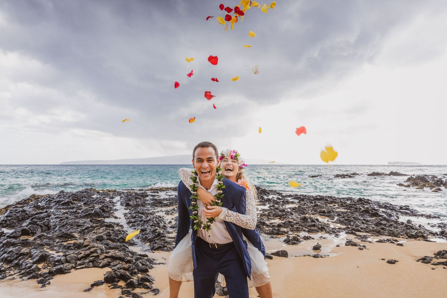 Colorful heart-shaped balloons float above couple during beach proposal.