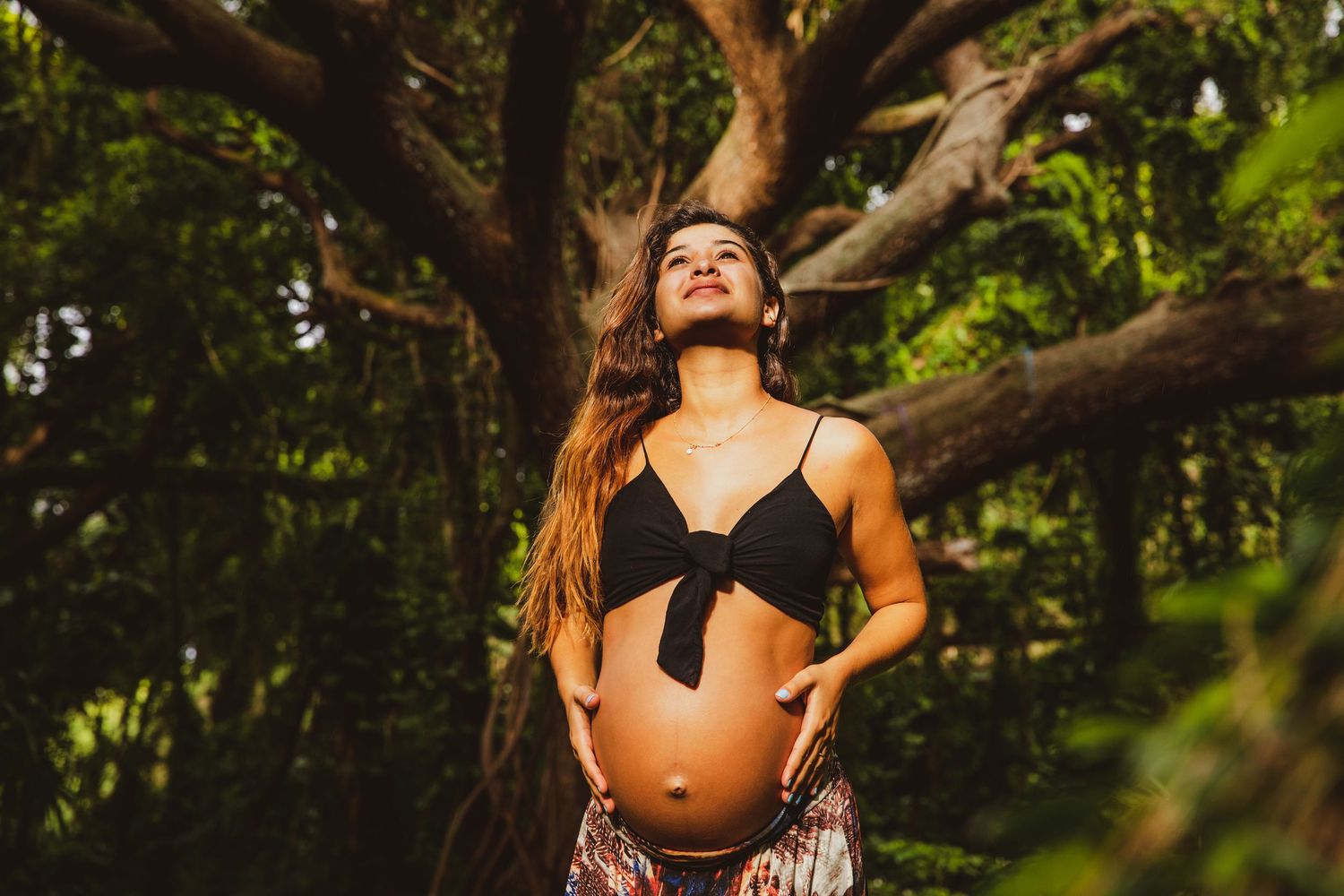 Candid maternity photo with sunlight streaming through forest trees.