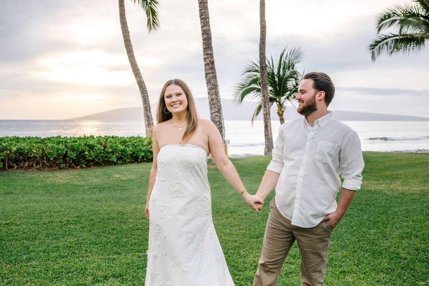 Couple strolls along manicured lawn with palm trees and ocean backdrop.