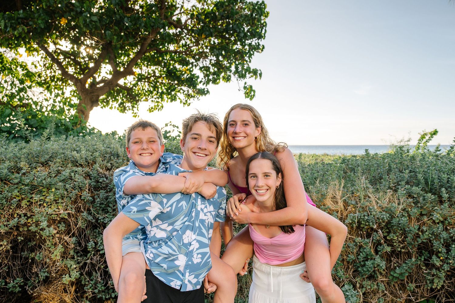 Family members sharing laughs and embraces during outdoor portrait session with natural lighting.