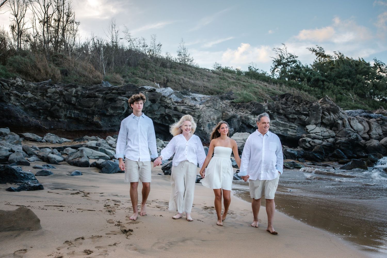 Family walking and posing along rocky beach coastline in white attire.