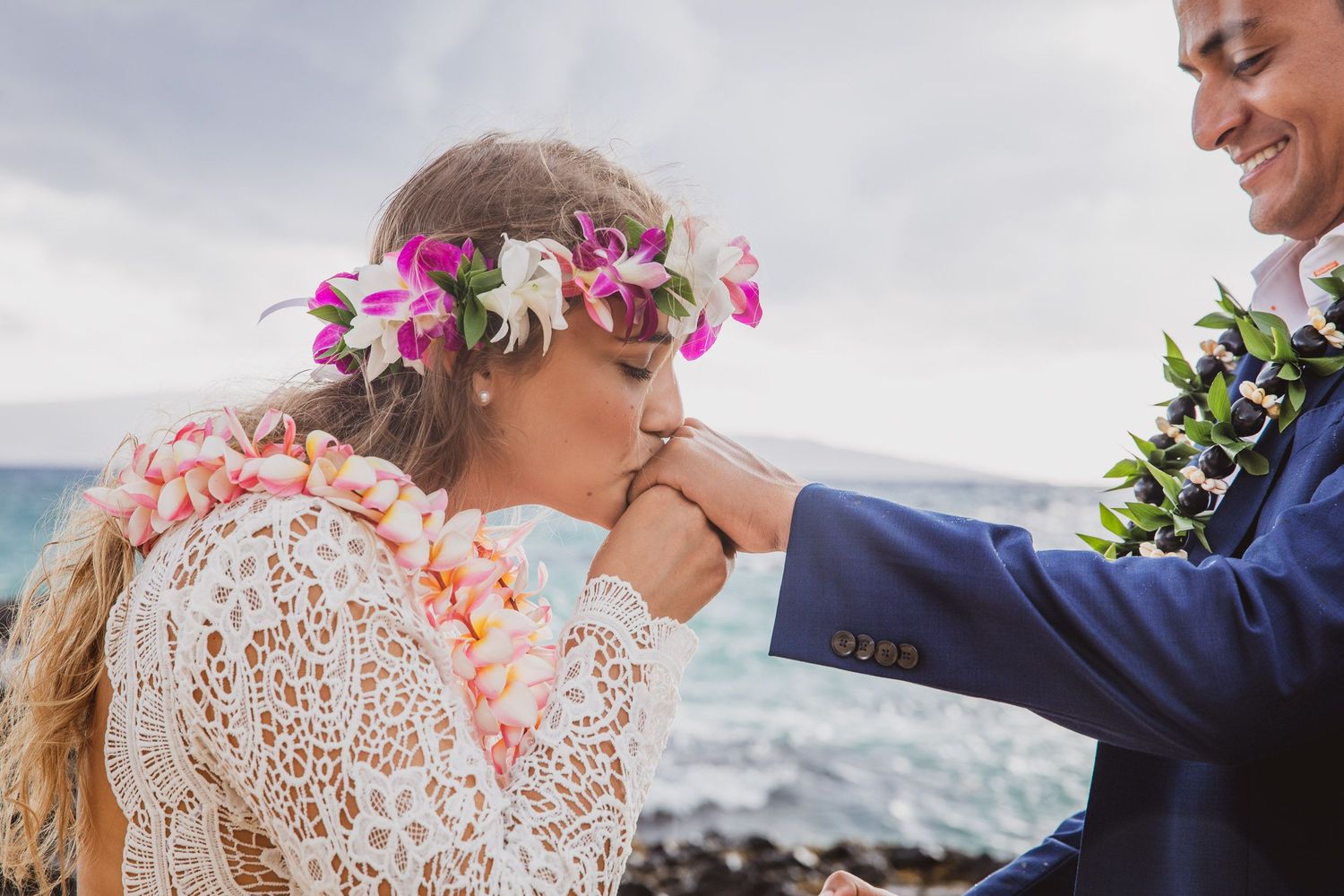 A tender wedding moment on a beach with floral crown and lace dress details.