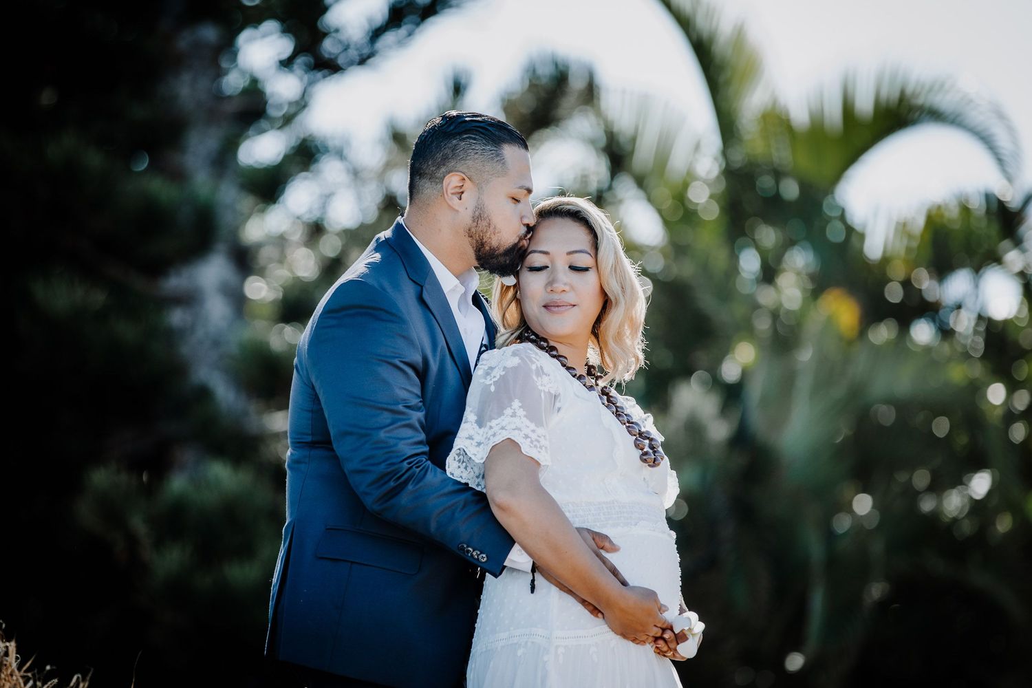 A romantic wedding couple embraces in a sunlit garden setting during their outdoor ceremony.