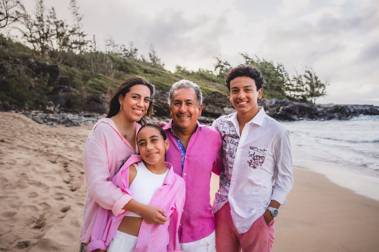 A cheerful family gathering on the beach wearing coordinated pink and white clothing.