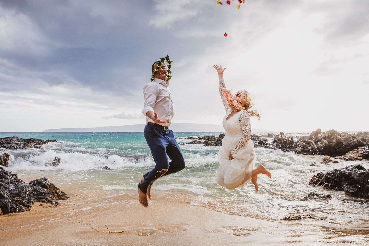 Playful moments captured at a beach wedding with balloons against a cloudy sky.