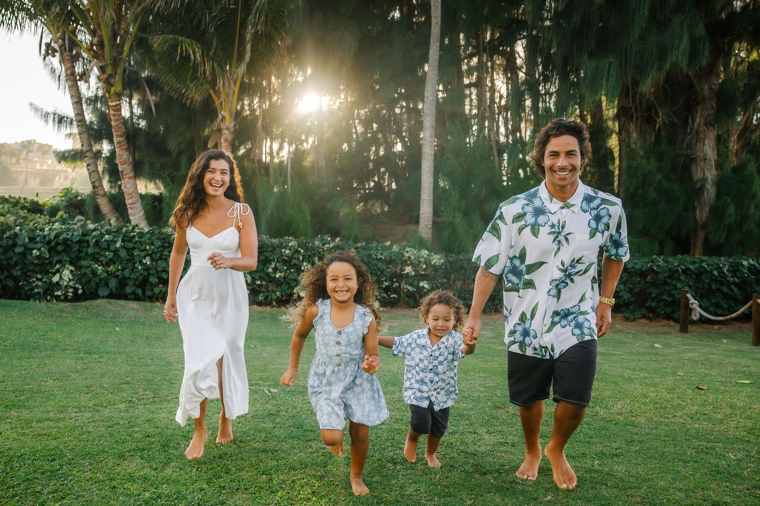 Family walking together on a grassy lawn during golden hour with sunlight filtering through trees.