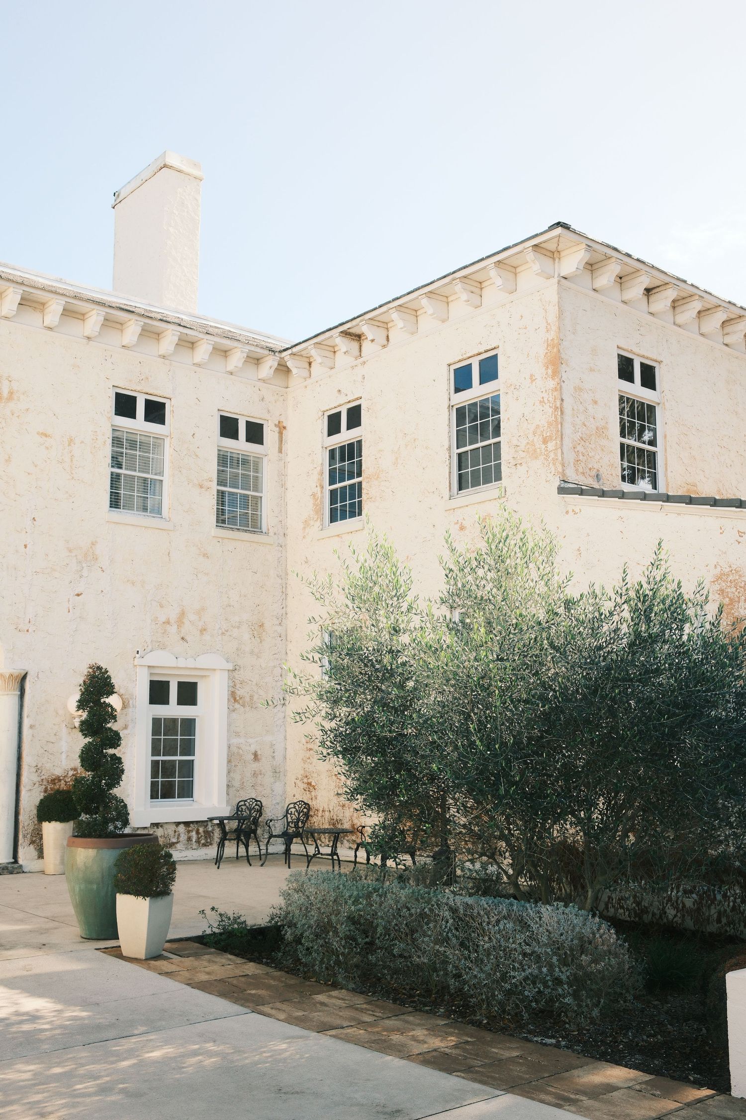 Exterior view of a Mediterranean-style white stone building with olive trees and modern windows.