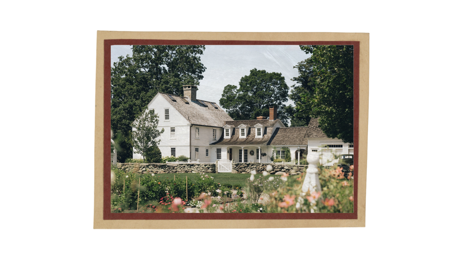 Framed photo of a charming white colonial farmhouse surrounded by lush gardens and tall trees in full bloom.