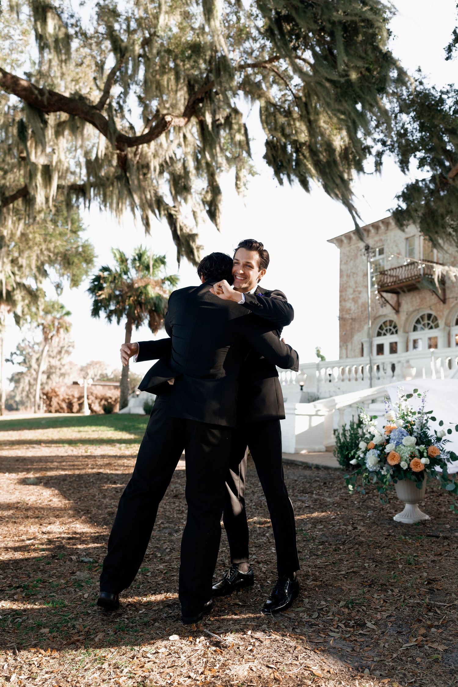 Wedding party members hugging and celebrating under Spanish moss draped trees.
