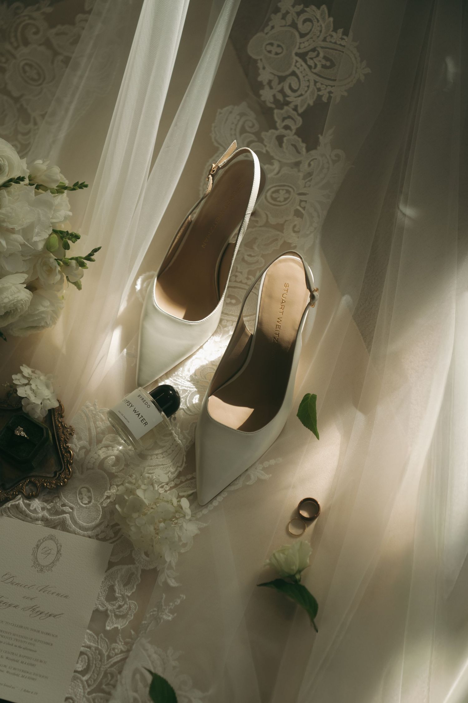 Elegant white bridal shoes and lace veil arranged artistically on a light surface with delicate floral details.