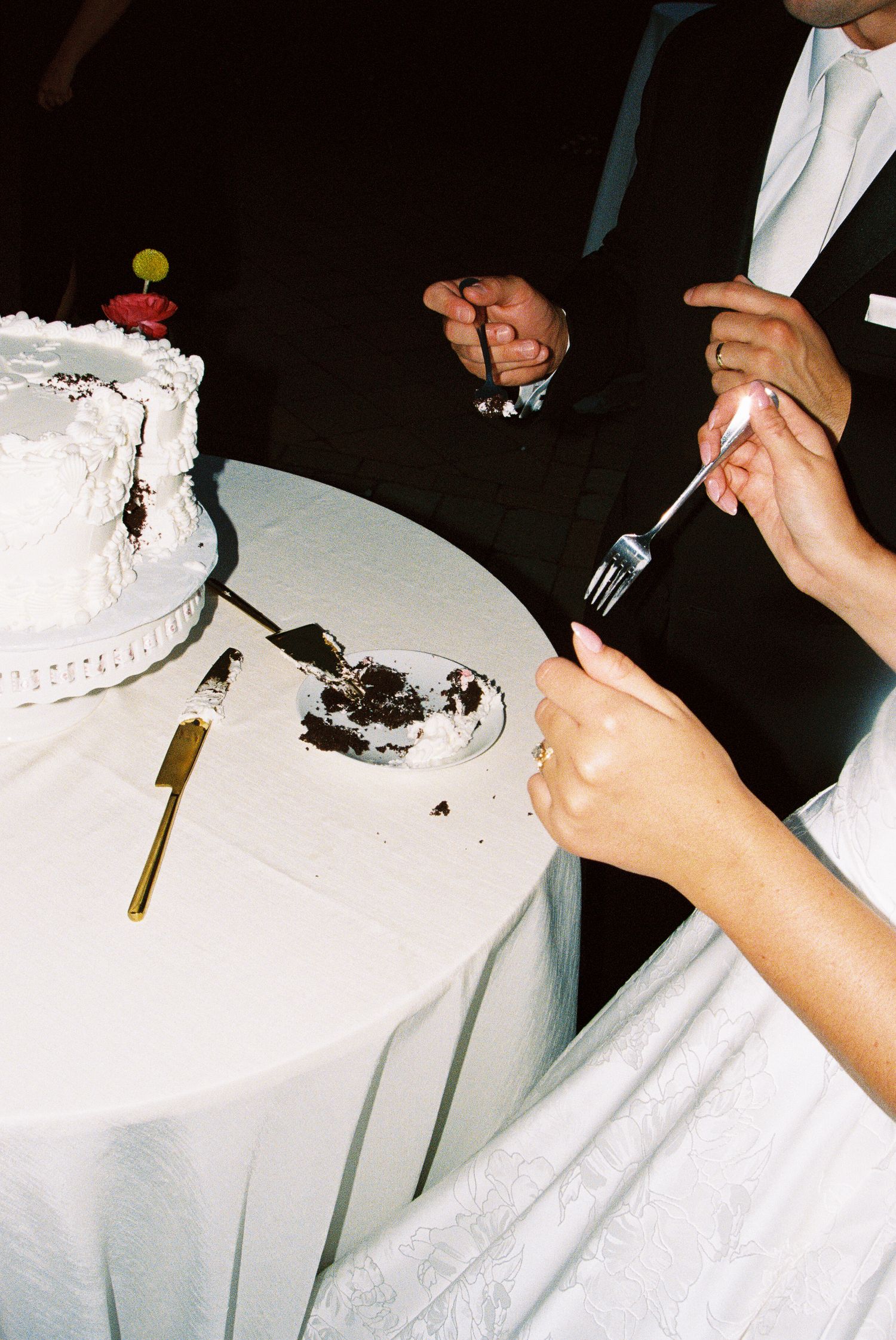 Newlyweds cutting a white wedding cake at a reception table with a gold knife and forks.