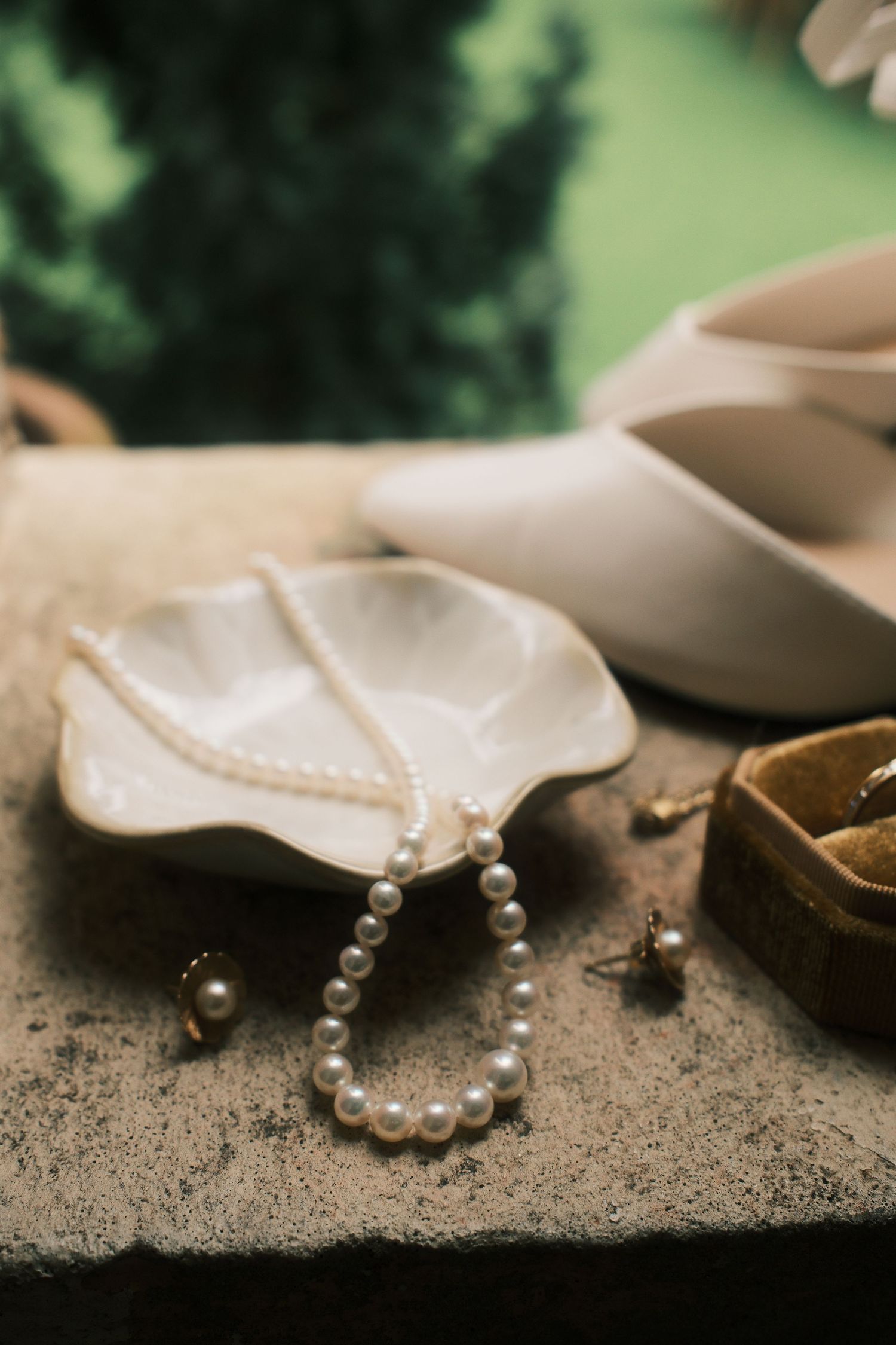 A pearl necklace and wedding accessories arranged on a stone surface with soft lighting.