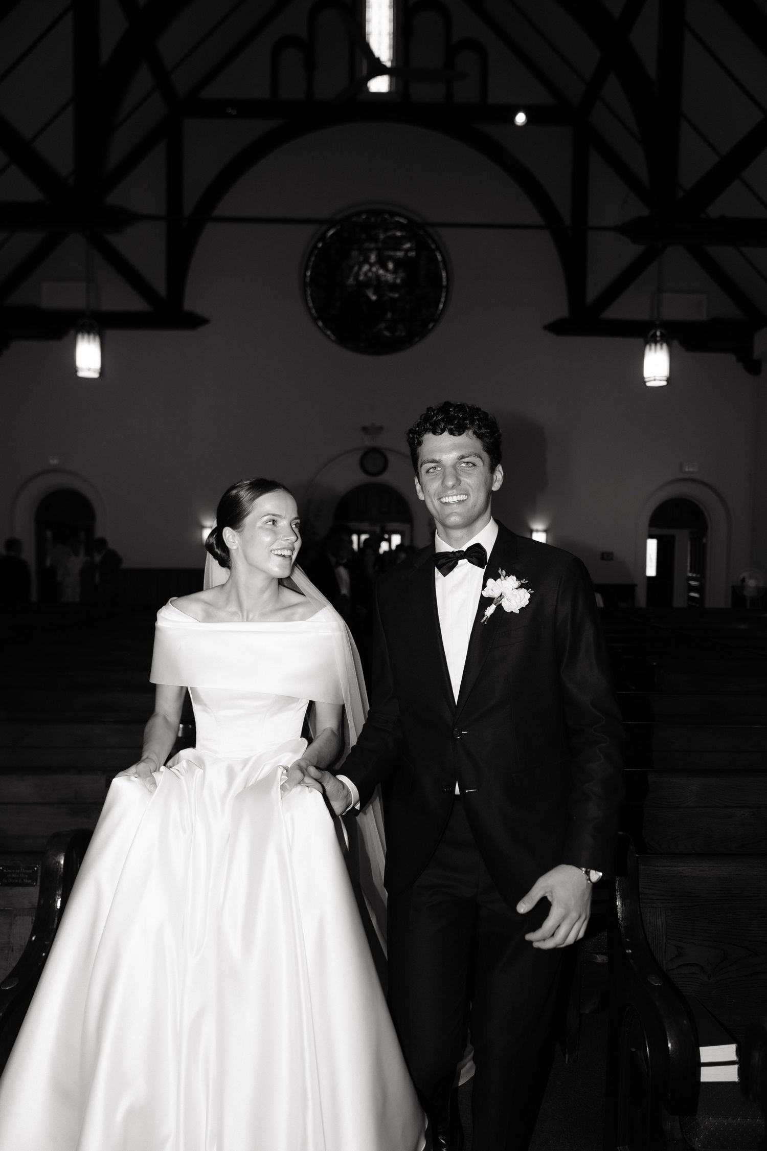 A black and white wedding photograph shows a bride in a white gown and groom in a tuxedo walking together.