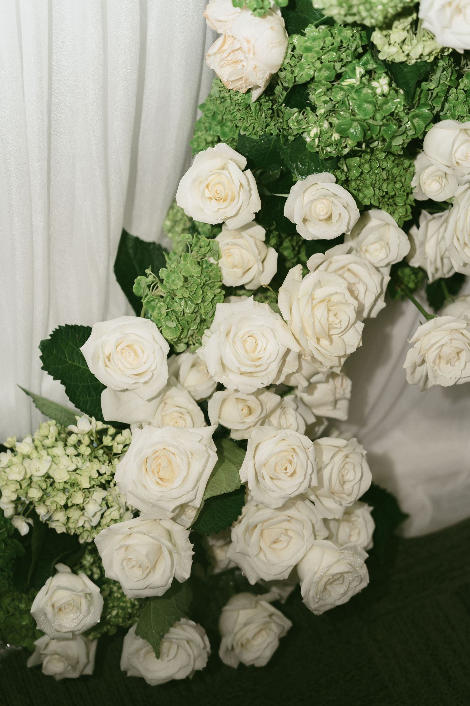 White roses and green hydrangeas create an elegant floral arrangement against a light background.